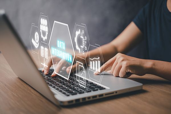 Hands typing on a laptop with digital icons showing data integration